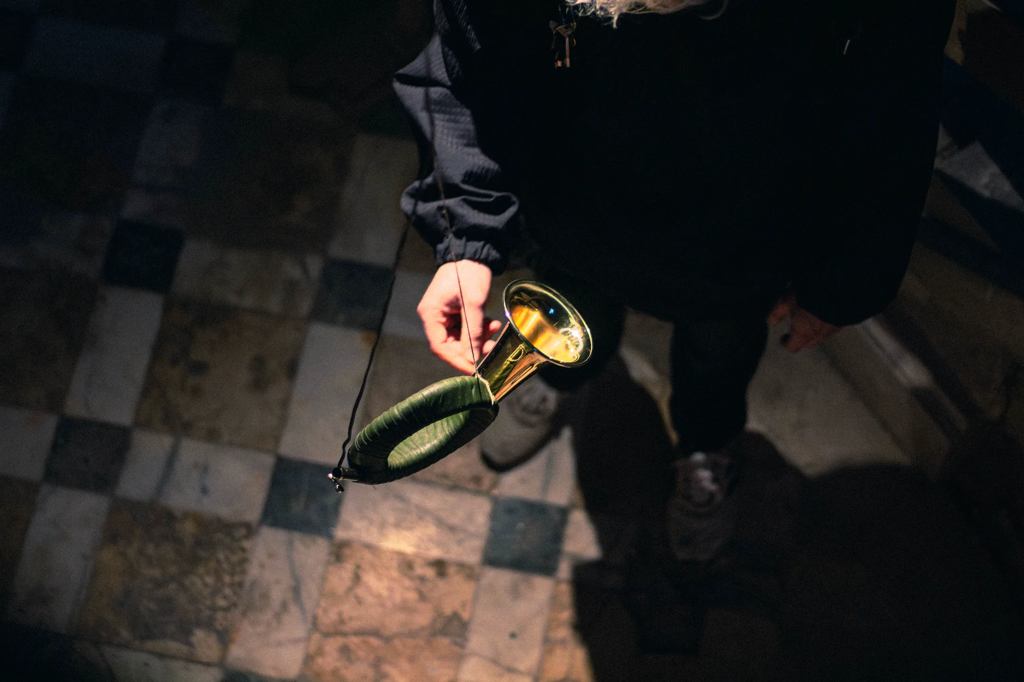 Visitor holding the green leather-wrapped hunting horn viewed from above, checkered stone tile floor, Hirsch Tot interactive sound installation Dessau