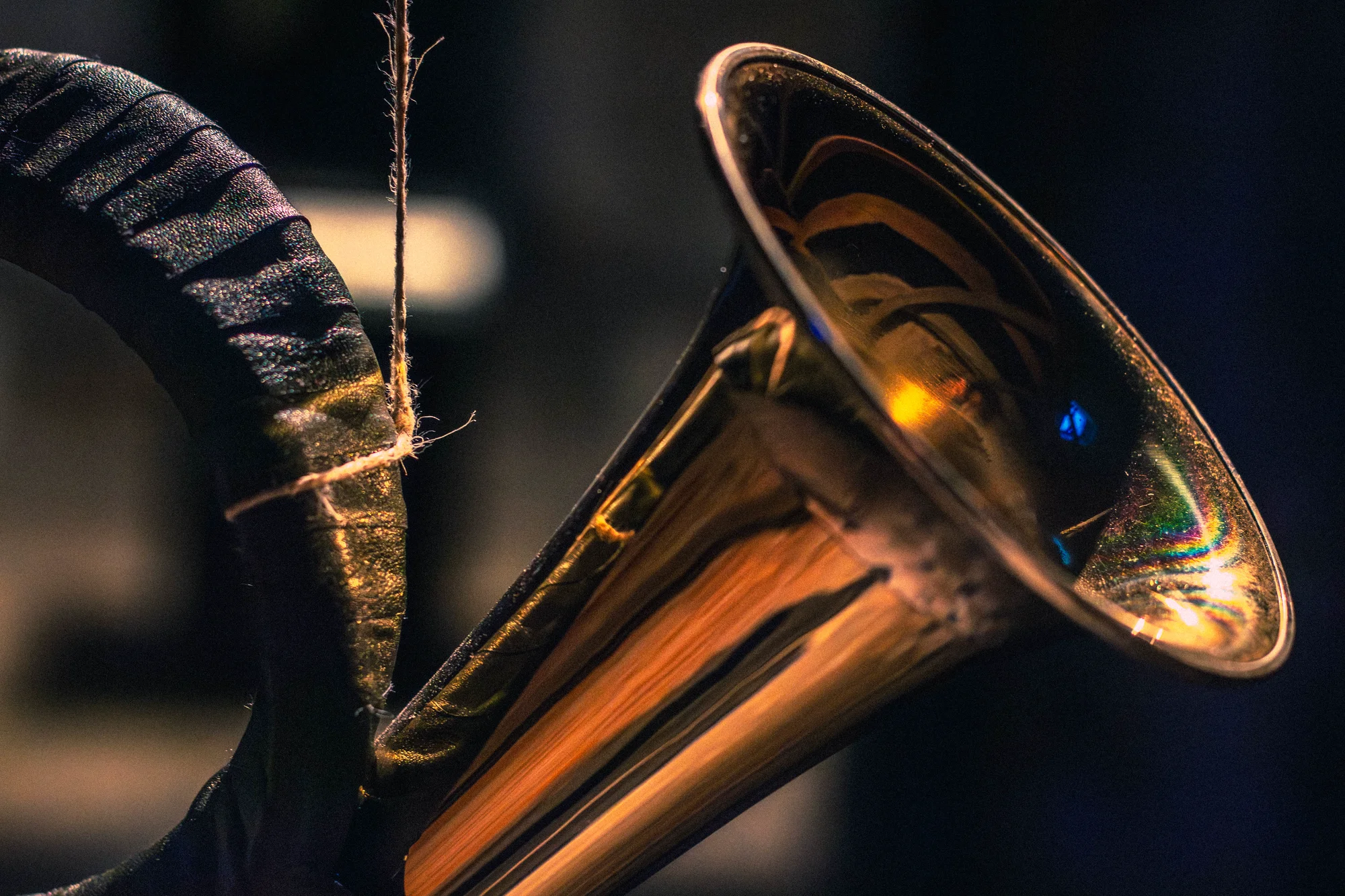 Macro close-up of brass hunting horn bell with colorful light reflections and frayed twine, dark leather-wrapped body, Hirsch Tot by Jacob Aran