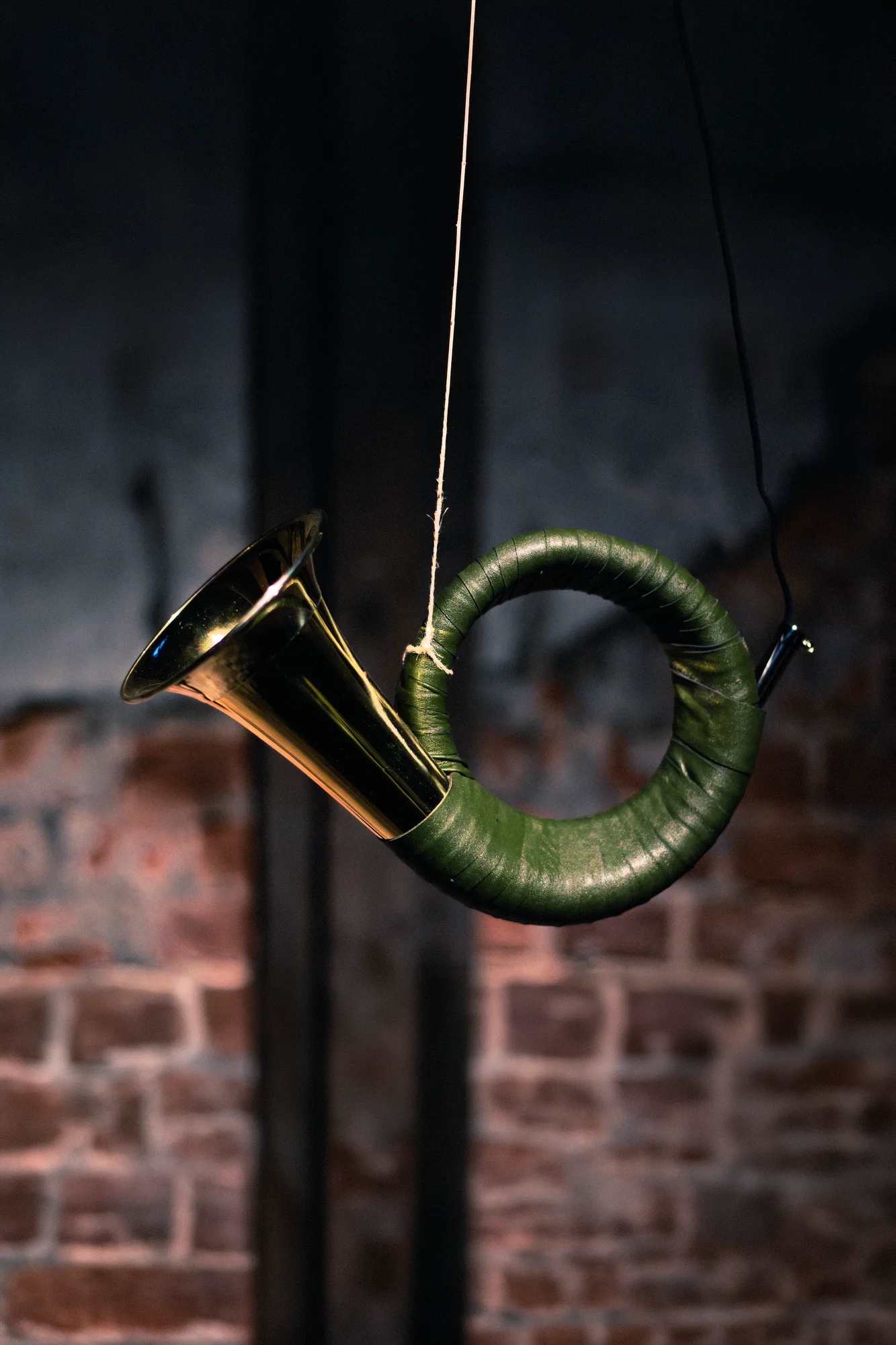 Green leather-wrapped hunting horn hanging vertically by string against exposed brick wall, Hirsch Tot installation at FEAST & ROADKILL Dessau